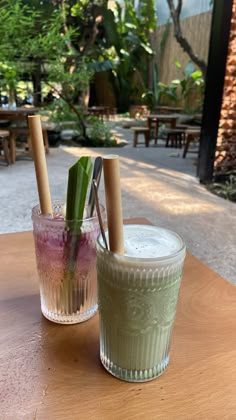 two glasses filled with drinks sitting on top of a wooden table next to each other