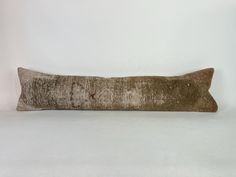 a brown and white pillow sitting on top of a white bed cover covered in flecky fabric