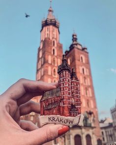 a person holding up a miniature model of a building in front of a tall tower