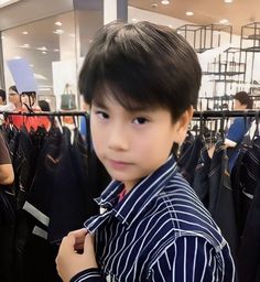 a young boy standing in front of a rack of clothes and looking at the camera