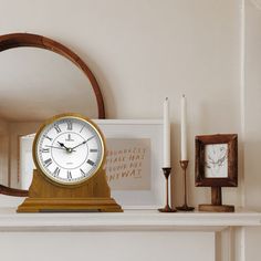 a clock sitting on top of a mantle next to two candles and a framed photograph