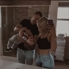 a man taking a selfie with two women in front of a bathroom mirror while holding a baby