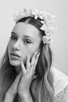 a woman with flowers in her hair wearing a white dress and holding her hand to her face