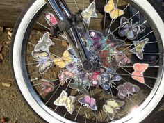 a bicycle wheel with butterflies painted on the front tire and spokes, sitting in dirt