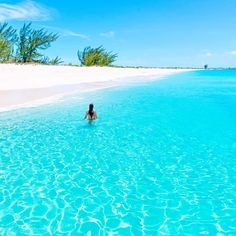 a person swimming in the ocean with clear blue water and white sandy beach behind them