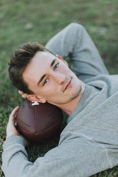 a man laying on the ground with a football in his hand and looking at the camera