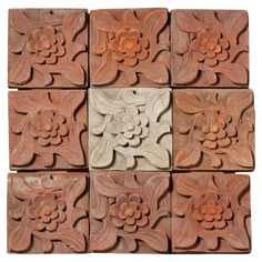 several square tiles with flowers and leaves on them, all made out of red clay