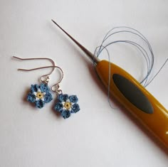 a pair of blue and yellow flower earrings sitting on top of a table next to a knitting needle