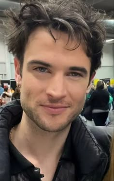 a close up of a person wearing a leather jacket and smiling at the camera with people in the background