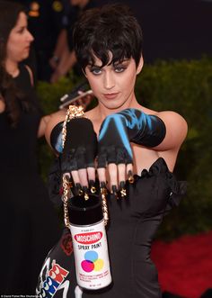 a woman in black dress holding up a bottle of tattoo ink and wearing gloves with chains around her arm