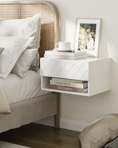 a nightstand with two books and a cup on it next to a bed in a bedroom