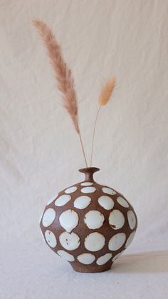 a brown and white vase sitting on top of a table next to a dry plant