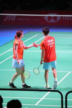 two people shaking hands on a tennis court with racquets in their hands