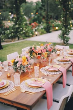 an outdoor table set with pink and yellow plates, place settings and flowers in vases