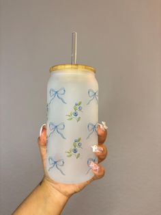 a hand holding a blue and white can with bows on it's lid, in front of a gray wall