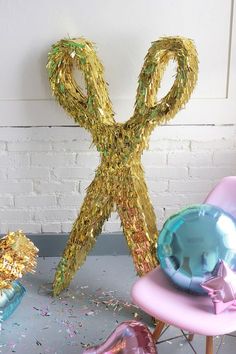 a pair of gold scissors sitting on top of a chair next to balloons and confetti