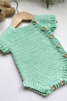 a green knitted baby romper with buttons on the front and bottom, next to a teddy bear