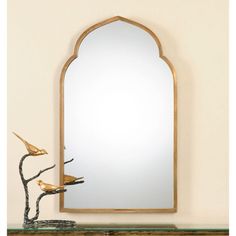 a mirror sitting on top of a wooden shelf next to a bird statue and a vase