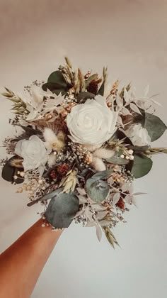 a bridal bouquet is being held by someone's hand with white flowers and greenery