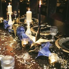 the table is set with candles, plates and napkins in blue and gold colors