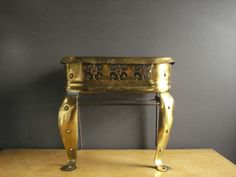 a gold table with an ornate design on the top and legs, sitting against a gray wall