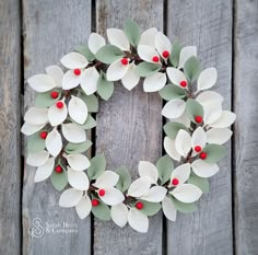 a white wreath with red berries and green leaves on a wooden background, ready to be used as a christmas decoration