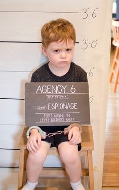 a little boy sitting on a chair holding a sign