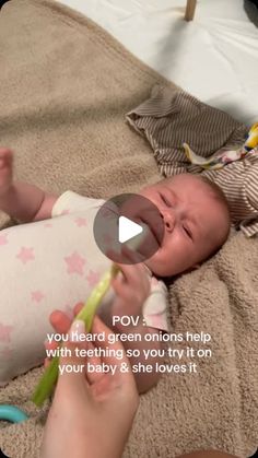 a baby laying on top of a bed holding a toothbrush