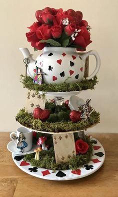 a three tiered tea pot with flowers and cards on the bottom, sitting on a wooden table