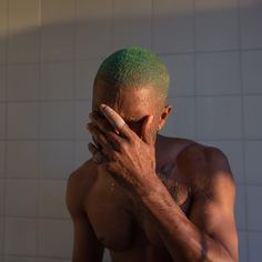 a shirtless man with green hair covering his face in front of a white tiled wall