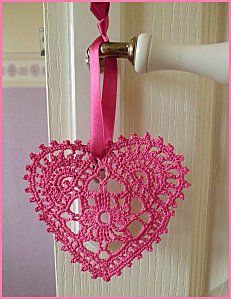 a pink heart hanging from a hook on a white door with a pink ribbon around it