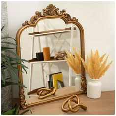 a mirror sitting on top of a wooden table next to a vase with some plants