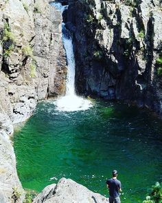 a man standing on top of a cliff next to a river filled with green water