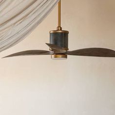 a ceiling fan with two blades hanging from it's side in front of a curtain