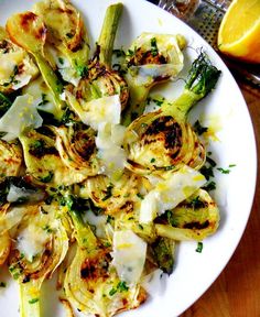 a white plate topped with grilled artichokes covered in cheese and herbs