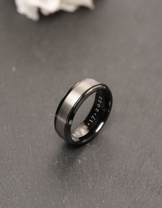 a black ring with the word trust engraved on it sitting next to a white flower