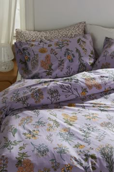 a bed with purple and yellow flowers on the comforter, pillows and pillowcases