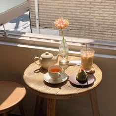 there is a small table with two cups on it and a tea pot next to the window