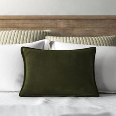 a close up of a pillow on a bed with white sheets and wood headboard