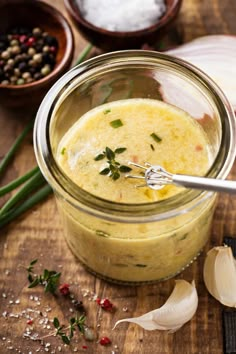 a glass jar filled with soup sitting on top of a wooden table next to garlic