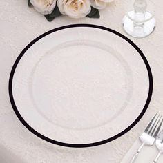 there is a white plate with black trim on it next to silverware and flowers