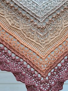 a crocheted shawl is shown in shades of brown, pink and white