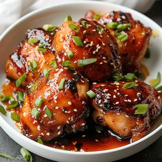 a white bowl filled with chicken covered in sauce and topped with sesame seeds, garnished with scallions