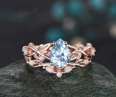 a ring with an aqua blue topazte surrounded by pink opal stones and leaves