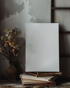 there is a vase with dried flowers next to an empty canvas on a table top