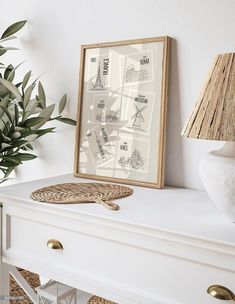 a white dresser topped with a lamp next to a plant