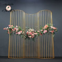 an iron gate with flowers hanging from it's sides in front of a gray wall