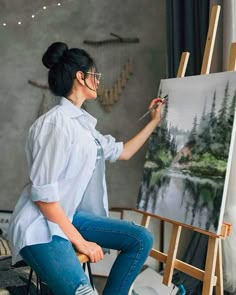 a woman is sitting on a chair and painting with an easel in front of her