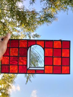 a hand holding up a stained glass window in front of a blue sky and tree