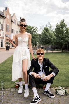 a young man and woman posing for a photo in front of a building with flowers on the ground